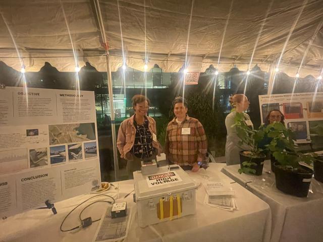 Michaela and Clare stand behind a table where the TARTA and a research poster are displayed