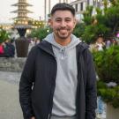 Alex is smiling standing outside in front of buildings and trees