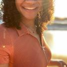 Photo of a person smiling with glasses on with the sun shining behind curly hair
